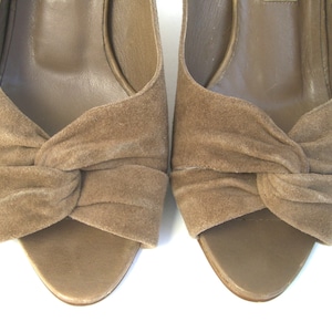 May include: A pair of light brown suede peep-toe heeled sandals with a knotted detail on the front.