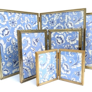 May include: Set of five gold-toned picture frames with a blue and white floral pattern. The frames are arranged in a staggered formation, with the largest frame at the back and the smallest frame at the front.