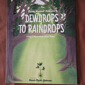 May include: A book cover for children, titled "DEWDROPS TO RAINDROPS", set in a forest scene. The cover features large trees and a small plant. The author is Darla Medeck-Johnson, and the illustrator is Kassie Pesch-Johnson. The book's subtitle is "A Drip's Trip to Make Sappy Happy."