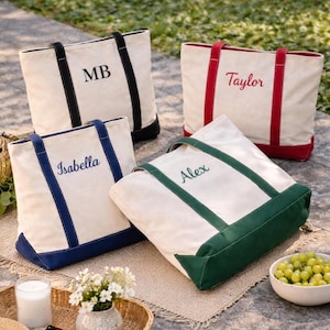 May include: Four canvas tote bags with personalized names or initials in various colors. The bags have a cream-colored body with colored accents on the handles and base. One bag has the initials "MB", another says "Taylor", and the others say "Isabella" and "Alex".