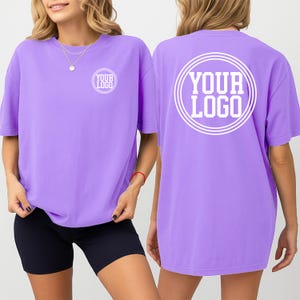 May include: A lilac-colored t-shirt with the text "YOUR LOGO" printed in white on the front and back. The shirt is a crew neck style and appears to be made of a soft material.