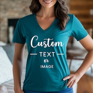 Peut inclure: T-shirt col en V de couleur teal avec le mot "Custom" en écriture cursive. En dessous du mot "Custom", le texte "TEXT or IMAGE" est en police sans-serif. Le t-shirt est de couleur teal unie.
