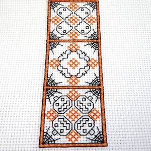 Puede incluir: Un patrón de punto de cruz con tres cuadrados naranja y negro. Cada cuadrado presenta un diseño diferente, incluyendo una telaraña, una calabaza y un patrón geométrico.