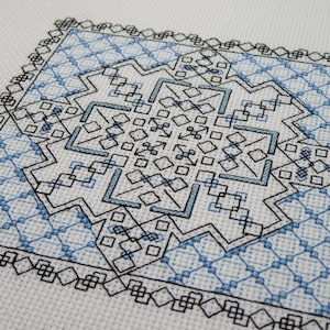 Könnte beinhalten: Ein schwarzes und weißes Kreuzstichmuster mit einem blauen und weißen geometrischen Design in der Mitte. Das Muster ist von einem schwarzen Rahmen umgeben.