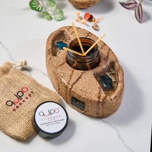 May include: A brown ceramic diffuser with a small glass jar filled with a dark liquid and wooden sticks. The diffuser is shaped like a rock and has a small, round opening for the jar. The jar is labeled "qulpo concept".