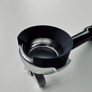 Könnte beinhalten: Ein verchromter Espresso-Siebträger mit schwarzem Griff und einem schwarzen, kreisförmigen Dosiertrichter, der oben auf dem Metallsieb sitzt. Der Siebträger hat eine polierte Metalloberfläche und ein sichtbares Sieb im Inneren des Korbes.