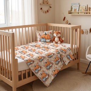 Può includere: Una culla in legno chiaro con un materasso bianco coperto da una coperta con un motivo ripetuto di zucche arancioni e blu e foglie autunnali. Un cuscino quadrato abbinato e un peluche a forma di volpe poggiano sul materasso.
