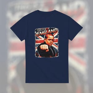 Puede incluir: Camiseta azul marino con un gráfico desgastado de una persona joven apretando el puño, sobre un fondo de la bandera británica. El texto "THIS IS ENGLAND" está encima de la imagen. Diseño de estilo vintage.