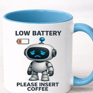 May include: White ceramic mug with a blue interior and handle. The mug features a sad robot illustration with the text "LOW BATTERY PLEASE INSERT COFFEE". The robot has blue eyes and a blue antenna.