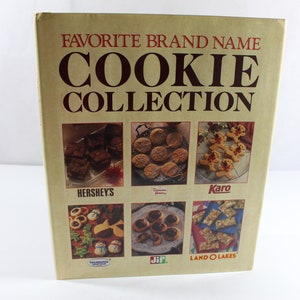 May include: A vintage cookbook titled "Favorite Brand Name Cookie Collection" with a beige cover and brown text. The cover features images of various cookies from Hershey's, Duncan Hines, Karo, and Land O'Lakes.