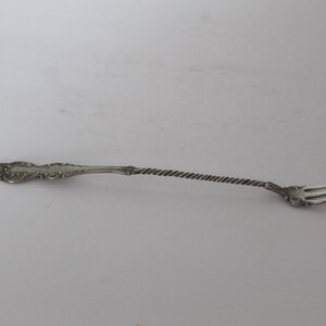 May include: A silver fork with an ornate handle and a twisted stem. The fork has three tines and is likely vintage. The handle has a decorative floral design.