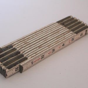 May include: A vintage folding ruler, measuring up to 6 inches. The ruler is made of wood with metal hinges and features inch markings. The numbers and markings are in black, and the wood has a worn, aged appearance.
