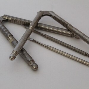May include: An assortment of antique silver nutcrackers and picks. The nutcrackers have textured handles and a hinged design. The picks are slender and pointed. The tools are arranged on a white surface.