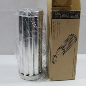 May include: A stainless steel Scalloped Bread Tube by The Pampered Chef, still in its original packaging. The cylindrical mold has vertical ridges and comes with a cardboard box featuring product details and a diagram.