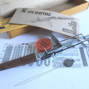 May include: A metal rug tufting tool with a brown wooden handle, accompanied by a small orange container of lubricant, a metal gauge, a printed instruction sheet labeled Rug Crafters Speed Tufting Tool, and a cardboard box.