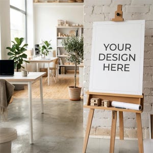 May include: A light-colored wooden easel holding a vertical white poster with the black text YOUR DESIGN HERE. The easel features a small shelf containing two miniature wooden house models and a white rolled paper tube resting on the ledge.