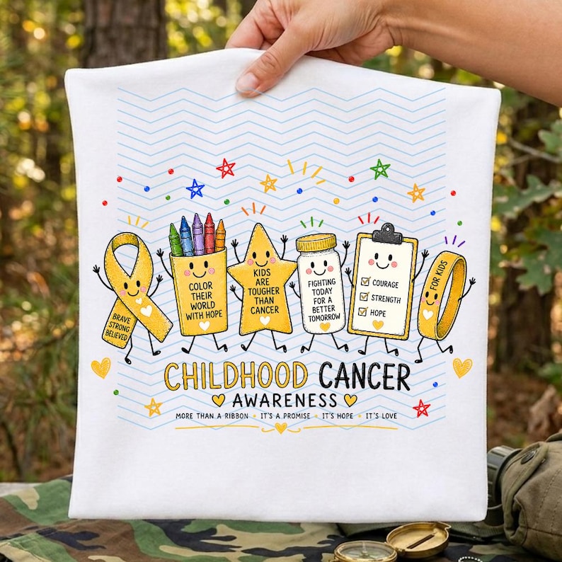 May include: A white t-shirt featuring a colorful graphic of a yellow awareness ribbon, a crayon box, a star, a jar, a clipboard, and a wristband with faces. Text reads CHILDHOOD CANCER AWARENESS, COLOR THEIR WORLD WITH HOPE, and more.