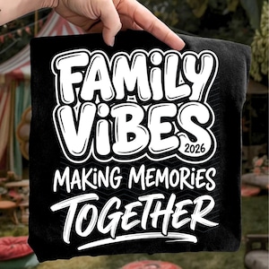 May include: Black t-shirt with the words "FAMILY VIBES 2026 MAKING MEMORIES TOGETHER" in white, bold, bubble letters. The shirt is held up by a hand, with a blurred outdoor background.
