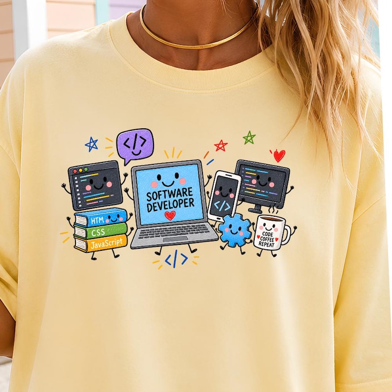 May include: A pale yellow t-shirt featuring a colorful graphic of a smiling laptop with the text SOFTWARE DEVELOPER, surrounded by animated computer monitors, a smartphone, a stack of books labeled HTML, CSS, and JavaScript, and a coffee mug.