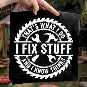 May include: Black t-shirt with a white circular graphic. The graphic features a saw blade border, wrenches, a hammer, and the text "THAT'S WHAT I DO, I FIX STUFF, AND I KNOW THINGS."