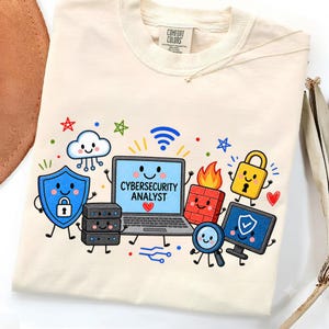 Puede incluir: Una camiseta de color crema con un gráfico colorido de elementos de ciberseguridad en estilo caricatura, que incluye un portátil con el texto CYBERSECURITY ANALYST, un escudo, una nube, un servidor, un cortafuegos, un candado y un monitor.