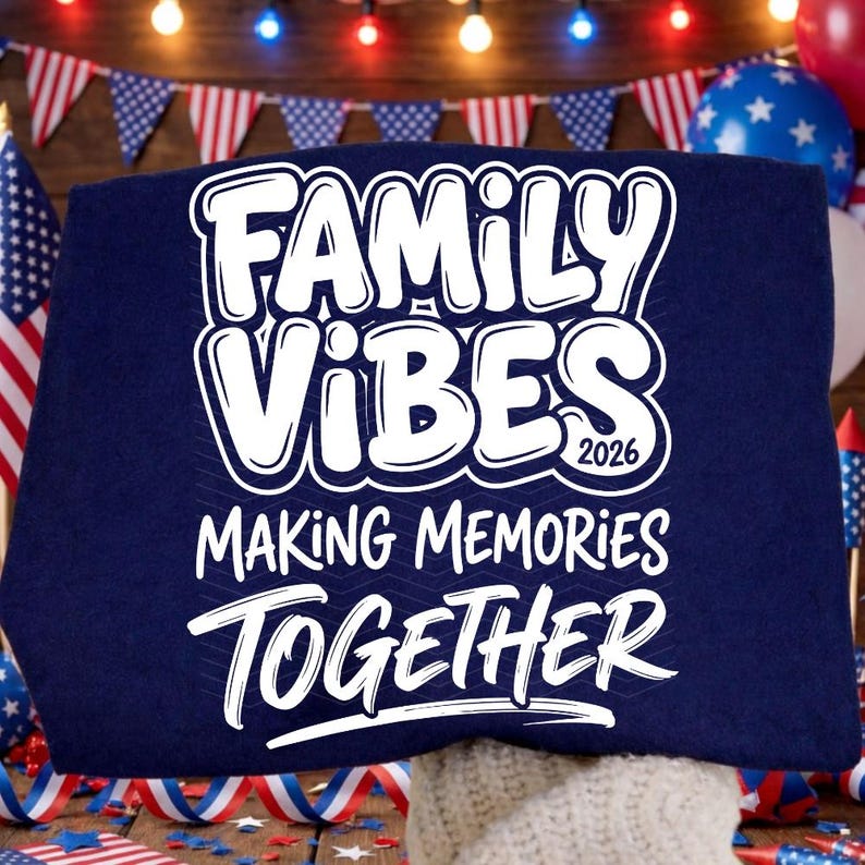 May include: A navy blue sweatshirt with the words "FAMILY VIBES 2026 MAKING MEMORIES TOGETHER" in white, outlined text. The sweatshirt is displayed with patriotic decorations in the background, including flags and balloons.