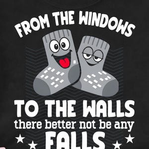 Op de afbeelding: Zwart T-shirt met de tekst "FROM THE WINDOWS TO THE WALLS there better not be any FALLS" en twee cartoon sokken. De sokken zijn grijs met witte accenten en hebben expressieve gezichten.