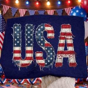 May include: A navy blue textile with the word "USA" stitched in red, white, and blue fabric, resembling the American flag. The letters are outlined with a frayed edge, and the background is decorated with a subtle zigzag pattern.