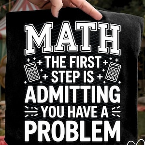 May include: Black t-shirt with the text "MATH + THE FIRST + STEP IS + ADMITTING YOU HAVE A PROBLEM" in white. The design includes calculator graphics. The shirt is held up by a hand.