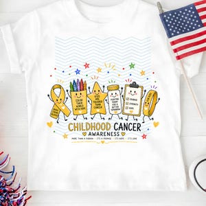 May include: A white t-shirt featuring a colorful graphic of cartoon characters including a yellow ribbon, a crayon box, a star, a medicine bottle, a clipboard, and a wristband. The text reads CHILDHOOD CANCER AWARENESS and includes motivational phrases.