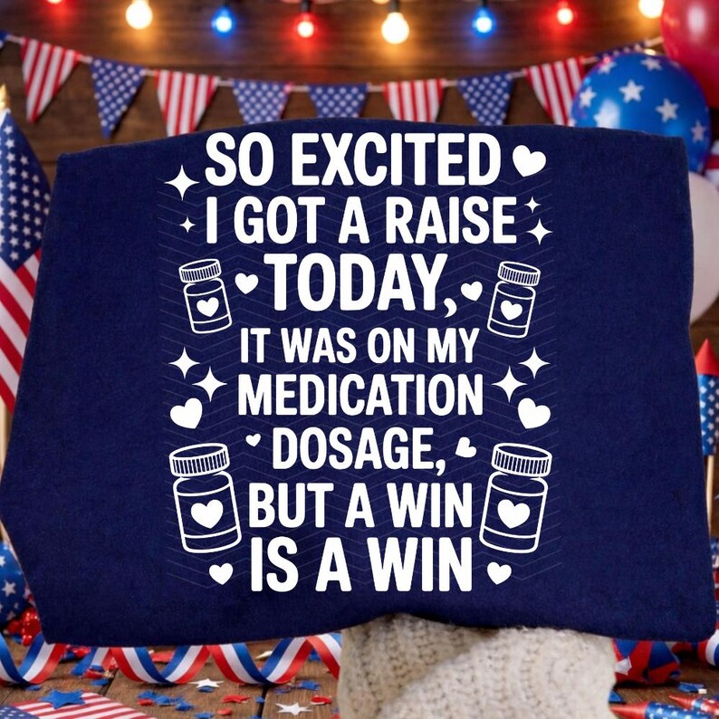 K&ouml;nnte beinhalten: Marineblaues T-Shirt mit wei&szlig;em Text: "SO EXCITED I GOT A RAISE TODAY, IT WAS ON MY MEDICATION DOSAGE, BUT A WIN IS A WIN." Das Design umfasst Herzen, Sterne und Pillenflaschen-Grafiken. Patriotisches Thema.