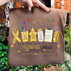 May include: A brown t-shirt featuring a Childhood Cancer Awareness graphic with a yellow ribbon, a crayon cup, a star, a medicine jar, a clipboard, and a wristband. The text reads: Color their world with hope, Kids are tougher than cancer, Fighting today for a better tomorrow, Courage, Strength, Hope, For kids, and More than a ribbon.