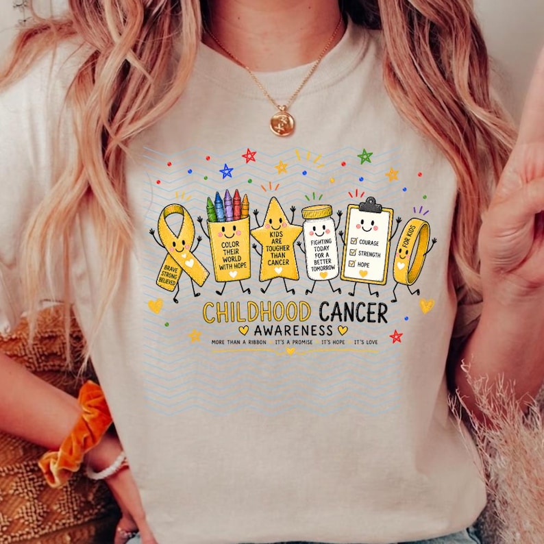 May include: A beige t-shirt featuring a graphic of cartoon items including a yellow awareness ribbon, a crayon cup, a star, a medicine bottle, and a clipboard. The text reads CHILDHOOD CANCER AWARENESS and includes phrases like COLOR THEIR WORLD WITH HOPE.