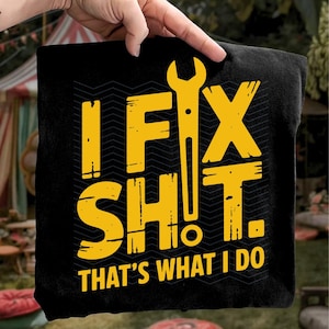 Puede incluir: Camiseta negra con texto amarillo y un gráfico de llave inglesa. El texto dice "IF FIX SH!T. THAT'S WHAT I DO" en una fuente en negrita y en bloques. El fondo tiene un sutil patrón de zigzag repetido.