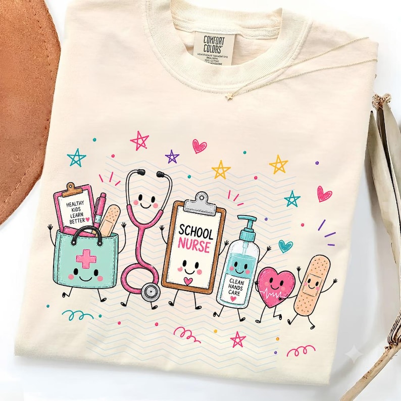 May include: A cream-colored t-shirt featuring a colorful graphic of a school nurse theme. The design includes a medical bag, a stethoscope, a clipboard labeled 'SCHOOL NURSE', a hand sanitizer bottle labeled 'CLEAN HANDS CARE', a heart, and a bandage.