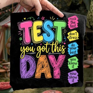 May include: Black t-shirt with colorful text: "TEST you got this DAY." Additional phrases include "rock the test," "don't stress," "do your best," "you know it," and "now show it." The design features bright pink, yellow, blue, green, and orange lettering.