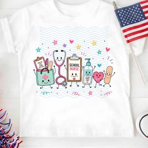 May include: A white t-shirt featuring a colorful graphic of anthropomorphic school nurse supplies including a stethoscope, clipboard labeled SCHOOL NURSE, hand sanitizer, heart, and bandage, set against a background of light blue wavy lines.