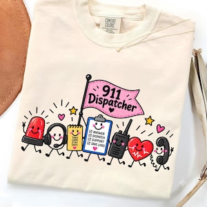 Könnte beinhalten: Ein cremefarbenes T-Shirt mit einer Grafik von Notruf-Dispatch-Gegenständen im Cartoon-Stil, darunter ein rotes Licht, Headset, Notizblock, Klemmbrett mit Text, Funkgerät, Herz und Telefon, unter einer rosa Flagge mit 911 Dispatcher.