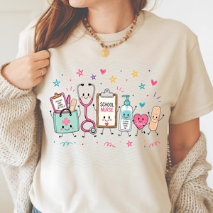 May include: A cream-colored t-shirt featuring a colorful graphic of cartoon medical items including a stethoscope, a clipboard labeled "SCHOOL NURSE," a hand sanitizer bottle labeled "CLEAN HANDS CARE," a heart, and a medical bag.