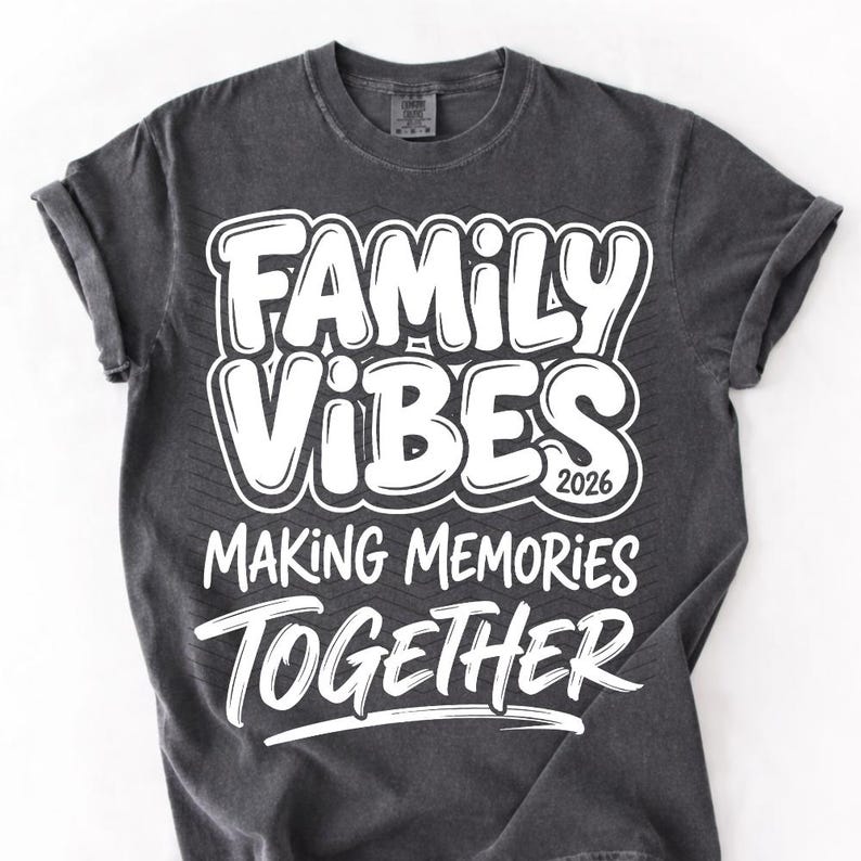 May include: Dark gray t-shirt with the words "FAMILY VIBES 2026 MAKING MEMORIES TOGETHER" in white, bold, bubble letters. The shirt has rolled-up sleeves and a crew neck.