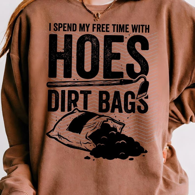 May include: A brown sweatshirt featuring the text "I SPEND MY FREE TIME WITH HOES DIRT BAGS" in black. The design includes a gardening hoe and a soil bag. The sweatshirt is a solid brown colour.