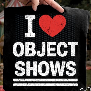 Könnte beinhalten: Schwarzes T-Shirt mit dem Text "I OBJECT SHOWS" in verblichener weißer Schrift. Eine rote Herzgrafik befindet sich über dem Wort "OBJECT". Zwei weiße horizontale Linien befinden sich unter dem Wort "SHOWS".