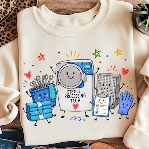 Op de afbeelding: Een crèmekleurig sweatshirt met ronde hals en een kleurrijke cartoonafbeelding van medische apparatuur met gezichtjes. Het ontwerp bevat een sterilisator met het opschrift STERILE PROCESSING TECH, een blauwe bak met instrumenten, blauwe handdoeken, een checklist en een blauwe handschoen.
