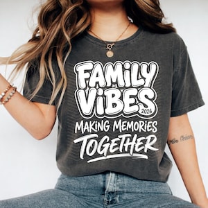 May include: Dark gray t-shirt with the words "Family Vibes 2026 Making Memories Together" in white, bold, bubble letters. The shirt is a crew neck and appears to be made of a soft, comfortable material.