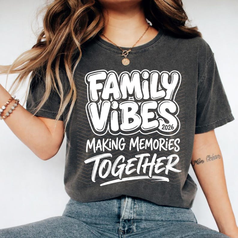 May include: Dark gray t-shirt with the words "Family Vibes 2026 Making Memories Together" in white, bold, bubble letters. The shirt is a crew neck and appears to be made of a soft, comfortable material.