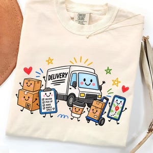 May include: A cream-coloured t-shirt featuring a graphic of a smiling delivery truck, cardboard boxes, a clipboard with a checklist, a coffee cup, and a smartphone. The text on the clipboard reads: DELIVER, PICK UP, MAKE PEOPLE SMILE.