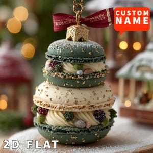 May include: A decorative Christmas ornament shaped like stacked macarons. The ornament features green and white layers with gold accents, cream filling, and decorative toppings. A red ribbon and gold cap are at the top. Text on the image reads "CUSTOM NAME" and "2D FLAT".