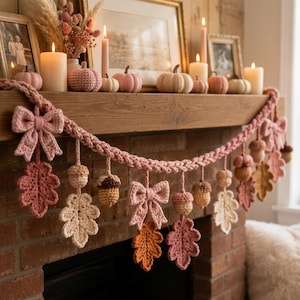 May include: A crocheted garland featuring pink bows, light pink and cream oak leaves, and small brown and tan acorns. The garland is draped across a wooden mantelpiece, with the crocheted elements hanging down in a repeating, decorative pattern.