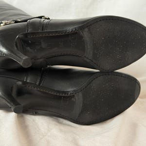 Peut inclure: Bottes hautes en cuir noir avec bout pointu et talon aiguille. Les bottes ont une boucle sur le dessus et une semelle textur&eacute;e. Les talons mesurent environ 7,6 cm de haut.