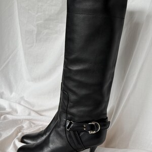 Peut inclure: Une paire de bottes hautes en cuir noir. Les bottes ont un bout pointu, un petit talon et une boucle autour de la cheville. Les bottes sont en cuir lisse et semblent en bon &eacute;tat.